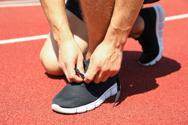 Omhoog sluiten de mensen bindende schoenveters op rode atletische renbaan ,.