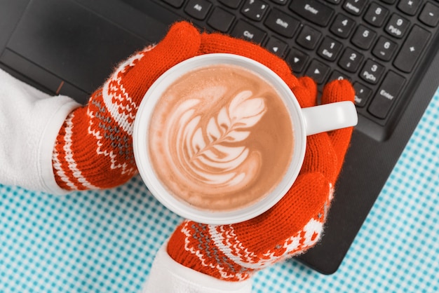 Ð¡omputer keyboard hands in warm gloves with cup of art coffee