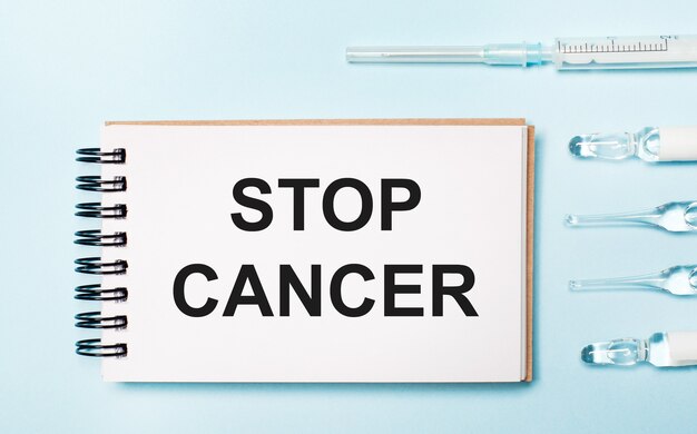 파란색 배경에 약이 있는 앰플과 Stop Cancer라는 텍스트가 있는 노트북. 의료 개념