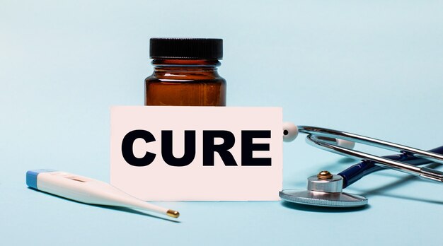 Фото На синем столе - флакон для таблеток, стетоскоп, электронный градусник и карточка с надписью cure. медицинская концепция