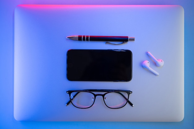 写真 色付きの背景に、ラップトップ、メガネ、ペン、ヘッドフォン、上面図。ビジネスコンセプト。