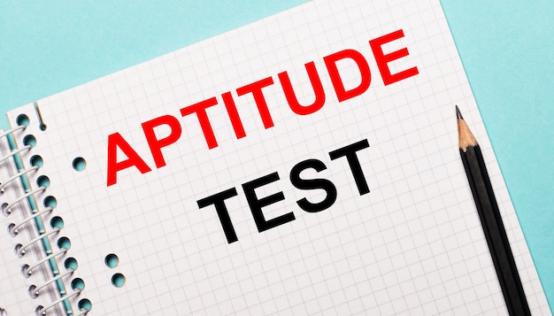 사진 하늘색 표면에 aptitude test라는 글자와 검은 색 연필이있는 체크 무늬 노트