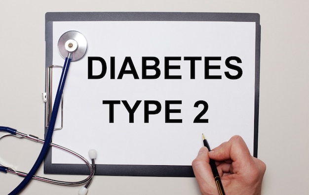 На светлой поверхности стетоскоп и лист бумаги, на котором мужчина пишет диабет типа 2. медицинское понятие.