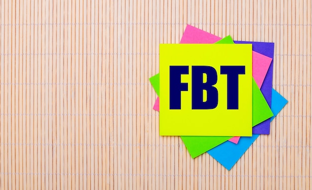 Фото На светлом деревянном фоне яркие разноцветные наклейки с надписью fbt fringe benefit tax.