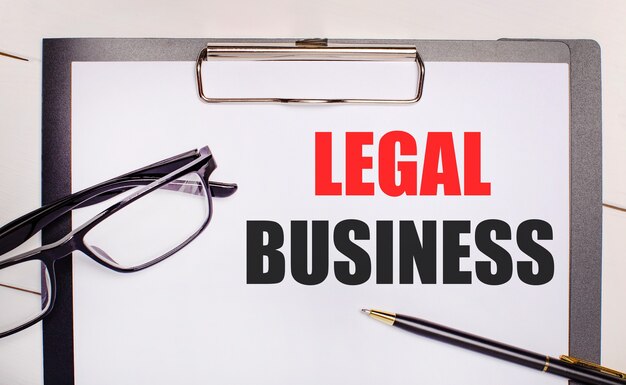 明るい木製の背景のメガネ、ペン、およびlegalbusinessというテキストが記載された1枚の紙。ビジネスコンセプト