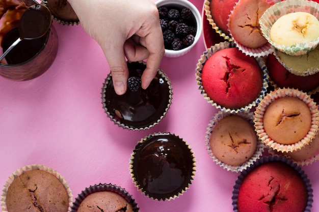사진 분홍색 배경에 한 여성이 컵케이크를 초콜릿과 딸기로 장식합니다. 부엌에서 수제 머핀