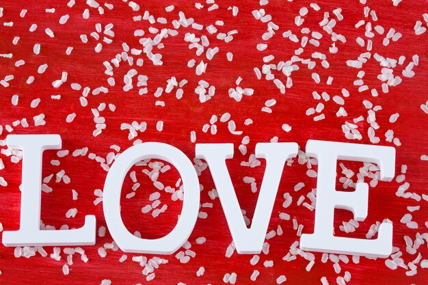 Фото На красном фоне лепестки вишни и декор белыми буквами: слово любовь