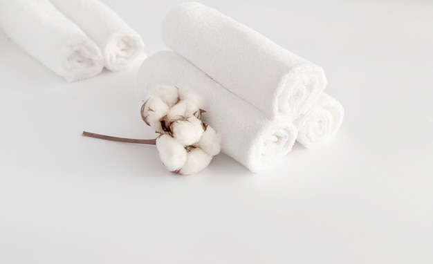 Фото На белом фоне в ролике сложены белые полотенца, ветка с хлопковыми цветами. концепция спа. концепция чистоты.