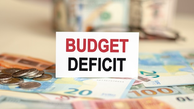 Фото На столе банкноты, пачка долларов и табличка с надписью - budget deficit.