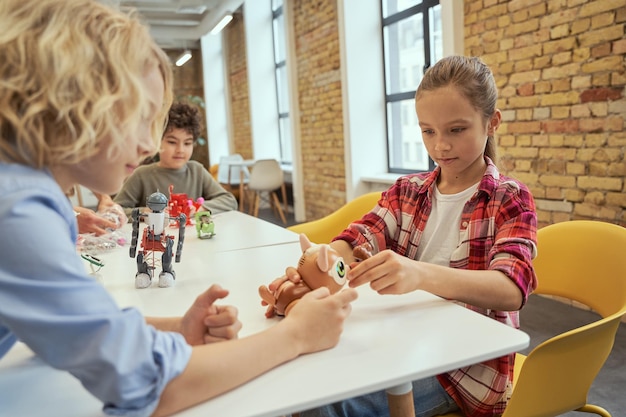 Onafhankelijke, oplettende kinderen die aan tafel zitten en technisch speelgoed onderzoeken terwijl