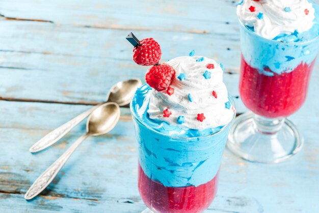 Onafhankelijkheidsdag. 4 juli. Gelaagd dessert van ijs, bessenframbozenmousse en slagroom, gedecoreerd in patriottische Amerikaanse stijl. Op een houten oude blauwe tafel. Kopieer ruimte