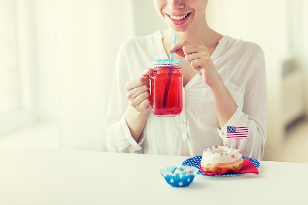 onafhankelijkheidsdag, viering, patriottisme en vakantieconcept - close-up van gelukkige vrouw die geglazuurde zoete donut eet, sap drinkt uit glazen glazen pot of mok en 4 juli thuis viert