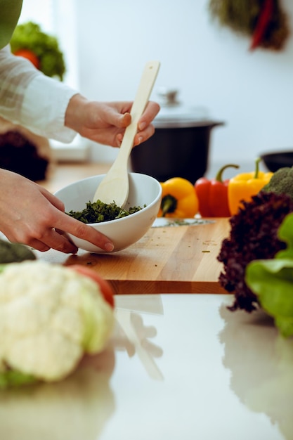 Onbekende menselijke handen koken in de keuken. Vrouw is bezig met groentesalade. Gezonde maaltijd en vegetarisch voedselconcept.