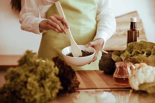 Onbekende menselijke handen koken in de keuken. Vrouw is bezig met groentesalade. Gezonde maaltijd en vegetarisch voedselconcept.