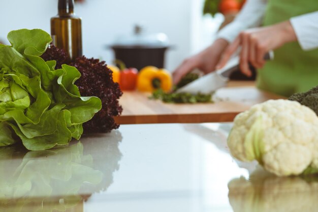 Onbekende menselijke handen koken in de keuken. Vrouw is bezig met groentesalade. Gezonde maaltijd en vegetarisch voedselconcept.