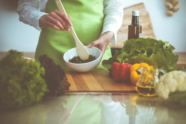 Onbekende menselijke handen koken in de keuken. Vrouw is bezig met groentesalade. Gezonde maaltijd en vegetarisch voedselconcept.