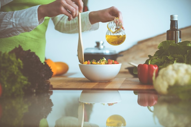 Onbekende menselijke handen koken in de keuken. Vrouw is bezig met groentesalade. Gezonde maaltijd en vegetarisch voedselconcept.