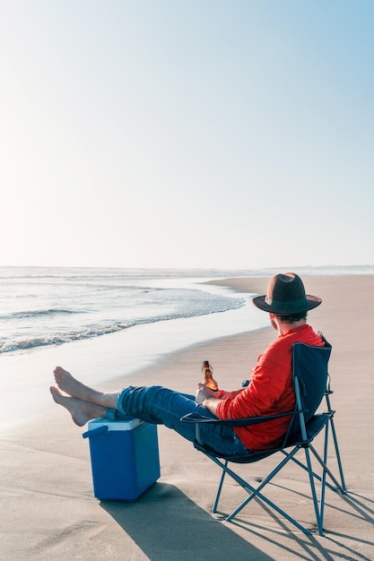 Onbekende persoon zit alleen in een stoel op het strand met een biertje of drankje ontspannen