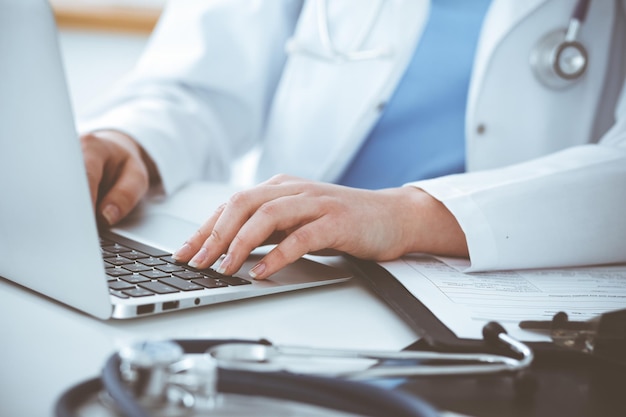 Onbekende vrouw-dokter die op laptopcomputer typt terwijl hij aan tafel zit. Geneeskunde concept.