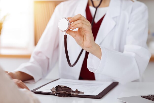 Onbekende vrouw-dokter met een stethoscoop in de handen in zonnige kamer, close-up van handen. Geneeskunde concept.