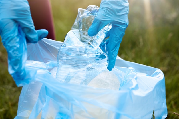 Onbekende vrouw oppakken van afval op de grond. vrouwelijke vrijwilligers die weidegebied schoonmaken, dame in blauwe handschoenen zet plastic fles in vuilniszak, mensen zorgen voor milieu.