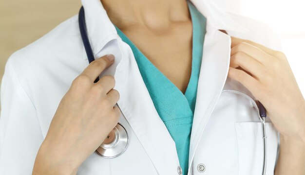 Onbekende vrouwelijke arts die zich met stethoscoop in zonnige kliniekclose-up bevindt