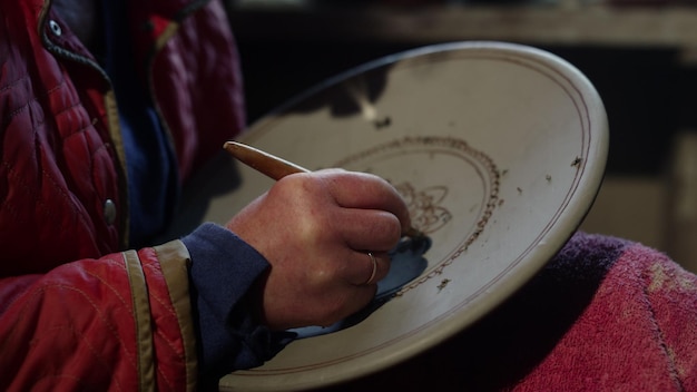 Onbekende vrouwelijke kunstenaar die met houten gereedschap werkt in een atelier Onbekende meester schraapt ornament in een studio Vrouwelijke handen maken decoratie op natte klei product in aardewerk