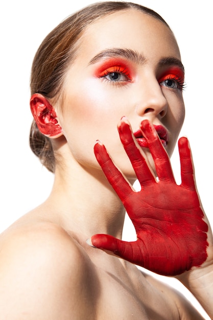 Onbewogen vrouwelijk model met rode lippen en oogschaduw permanent met geschilderde hand op witte achtergrond in de studio en wegkijken