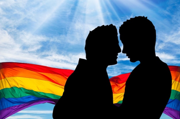Ð¡oncept of gay people. Silhouette of two gay men hugging each other against the backdrop of a rainbow flag