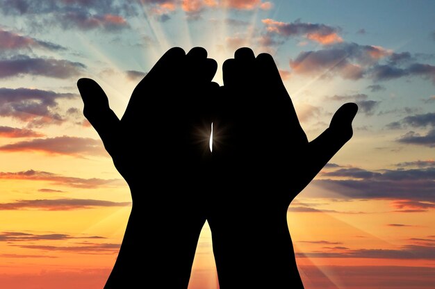 ¡oncept dell'islam, il corano. silhouette di mani in preghiera rivolte verso il cielo al tramonto