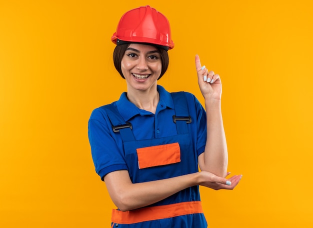 Onder de indruk jonge bouwvrouw in uniforme punten naar boven geïsoleerd op gele muur