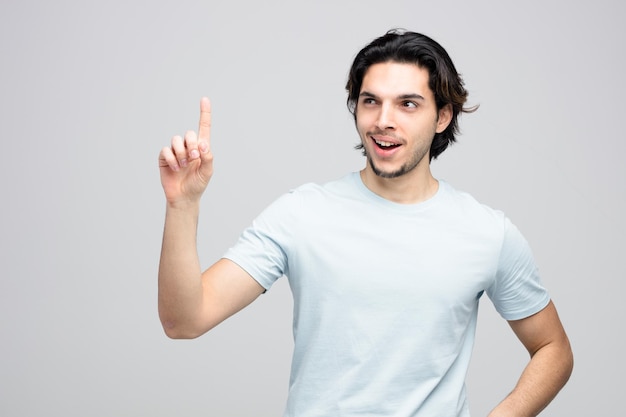 Onder de indruk van de jonge knappe man die naar de zijkant kijkt en omhoog wijst geïsoleerd op een witte achtergrond