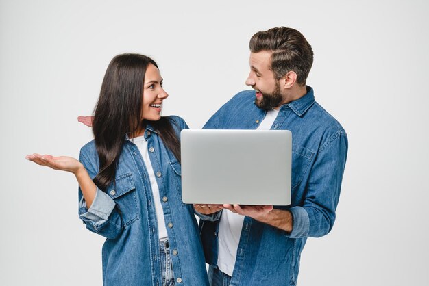 Foto onder de indruk, verrast, blank jong echtpaar echtgenoten vrouw en man gebruiken laptop voor online bijeenkomsten, werken op afstand, kijken naar webinars, e-leeren, spelen games, geïsoleerd in het wit.