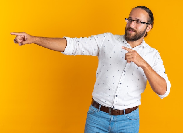 Onder de indruk volwassen knappe man met een bril die naar de zijkant kijkt en je gebaar doet geïsoleerd op een oranje muur