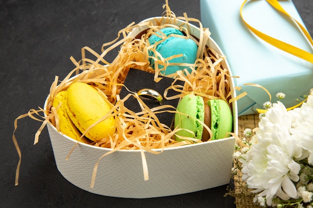 Onderaanzicht hartvormige doos met macarons verlovingsring cadeau bloemboeket op donkere achtergrond