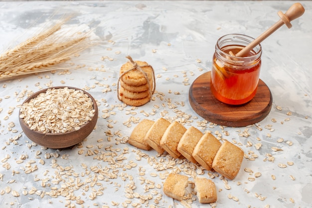 Onderaanzicht houten kom met haver tarwe spikes verspreide haver koekjes honing stok op honingpot op tafel