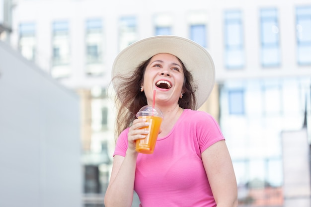 Onderaanzicht portret van een jonge mooie vrolijke vrouw in een hoed, wandelen door de stad met sap