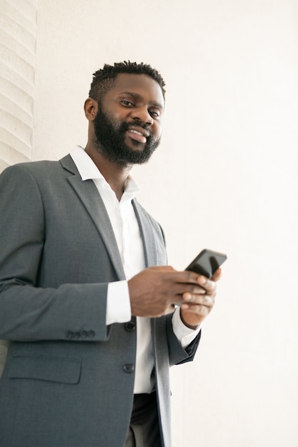 Onderaanzicht van lachende Afro-Amerikaanse bebaarde zakenman met behulp van messenger voor online communicatie op de telefoon