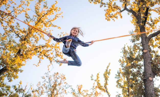 Onderaanzicht van meisje op trampoline springtouwen op blauwe lucht en herfst boomtoppen achtergrond