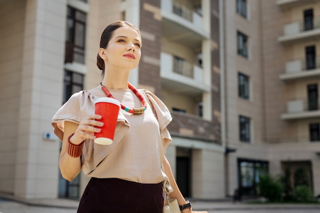 Onderbreken van het werk. Leuke jonge vrouw die van haar drankje geniet tijdens een koffiepauze op het werk