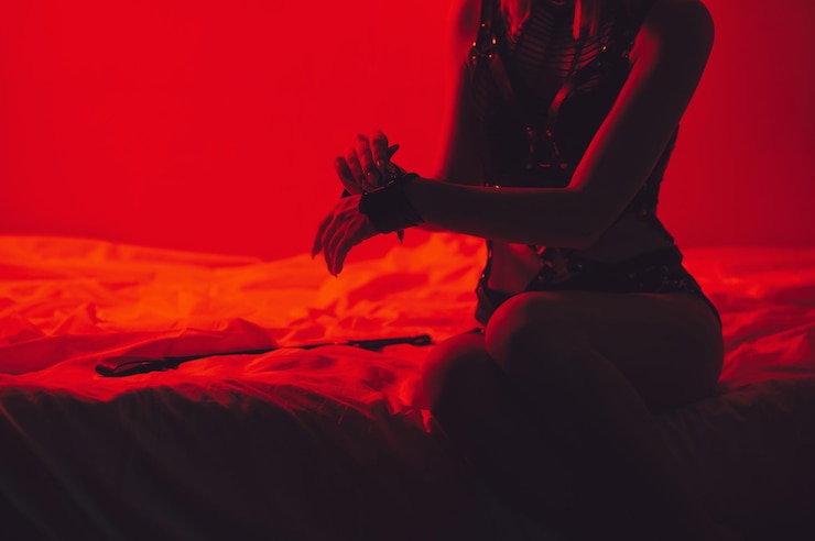 Foto onderdanige sexy vrouw in ondergoed zittend op het bed zet handboeien op haar handen in de slaapkamer bdsm concept van seks