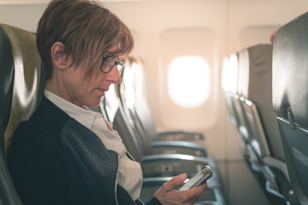 Onderneemster die bericht met mobiele telefoon verzendt terwijl het zitten in het vliegtuig vóór vertrek.