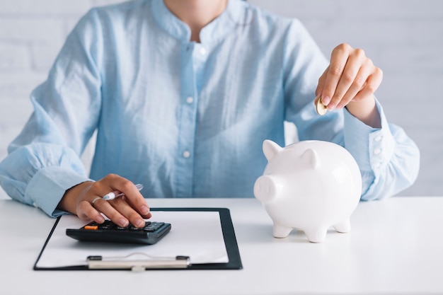 Foto onderneemster die calculator gebruiken terwijl het opnemen van muntstuk in piggybank op het werk