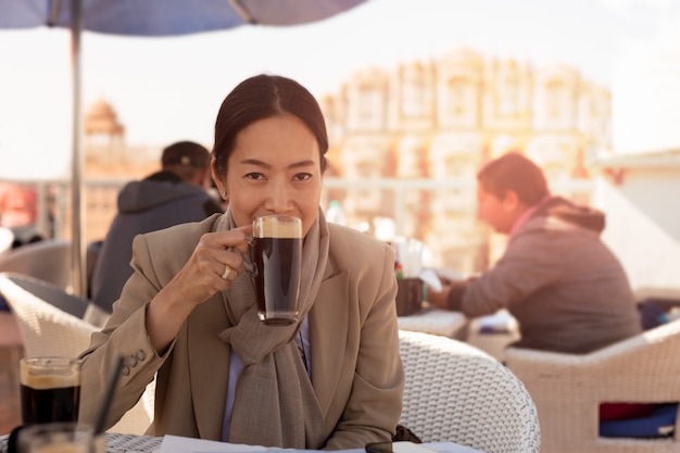 Onderneemster die een kop van koffie openluchtkoffie hebben die camera bekijken.