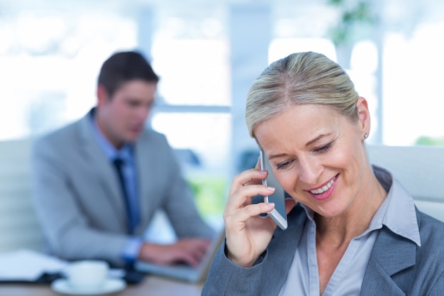 Onderneemster die een telefoongesprek met collega op achtergrond heeft