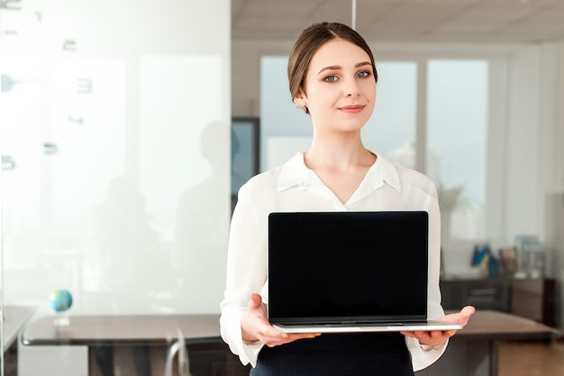 Onderneemster die het lege laptop scherm in het heldere moderne bureau toont