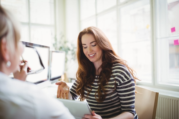 Onderneemster die laptop met behulp van terwijl het bespreken met collega in creatief bureau