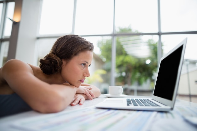 Onderneemster die op bureau leunt en laptop bekijkt