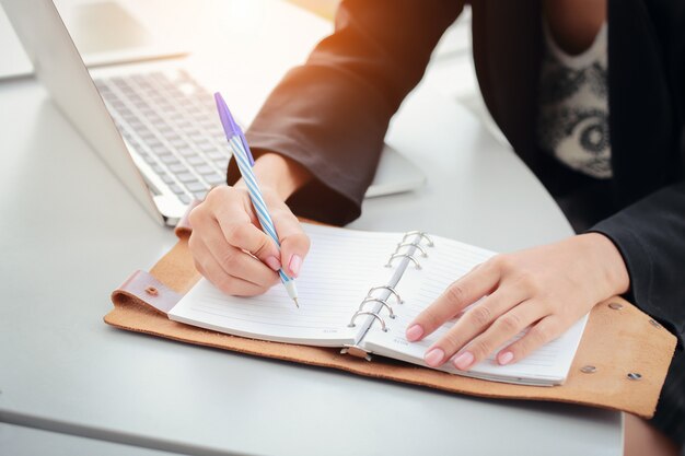 Onderneemster die op notitieboekje met laptop computer schrijft