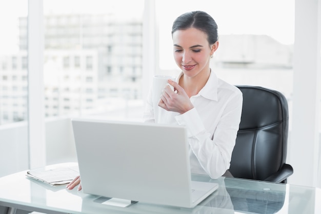 Onderneemster het drinken koffie terwijl het gebruiken van laptop bij bureau